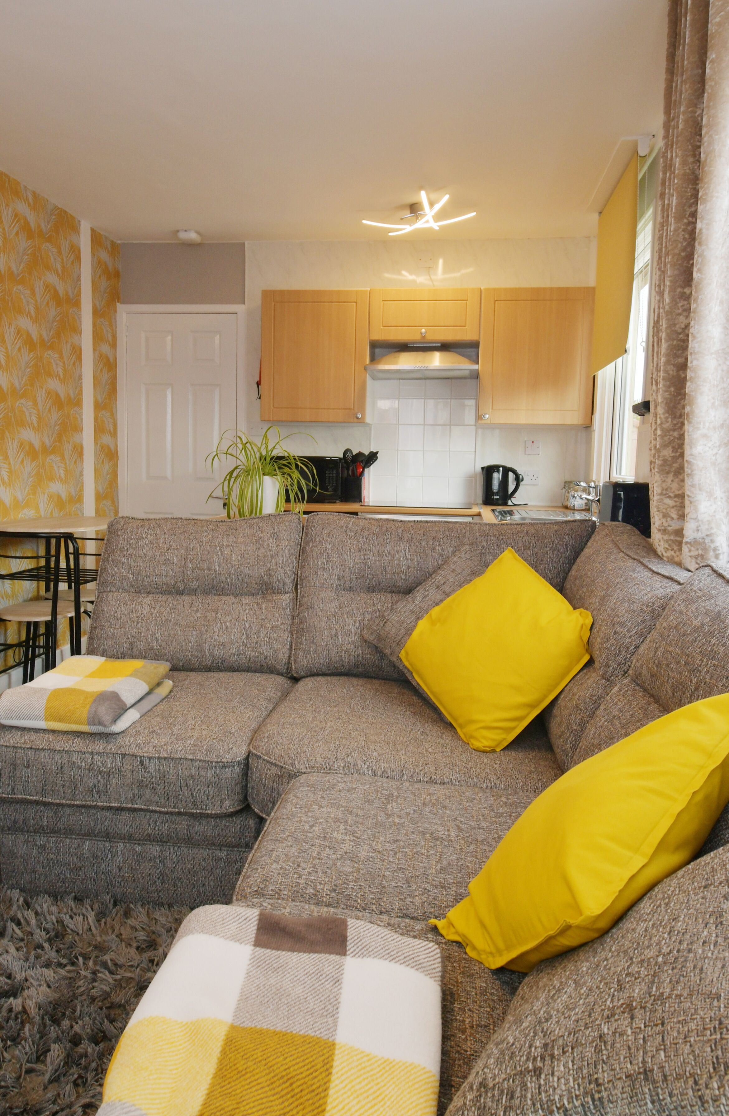 Een woonkamer met een grijze modulaire bank, gele kussens en een geruit plaid.