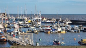 Un puerto deportivo con varias embarcaciones amarradas, un muro de ladrillo en primer plano y un cielo despejado.