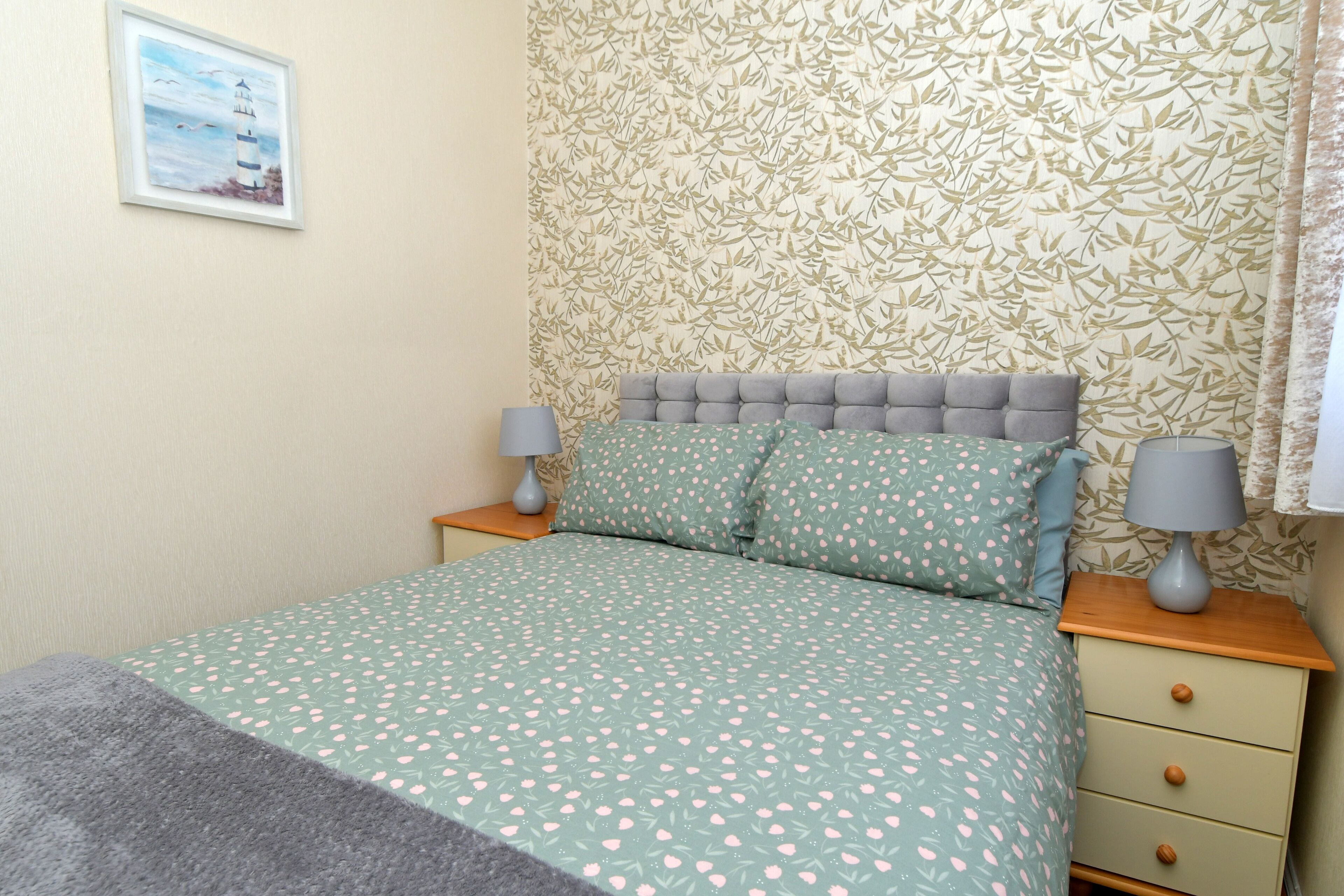 Un dormitorio con una cama, dos mesitas de noche, una lámpara sobre cada mesita y una pared con un diseño de hojas.