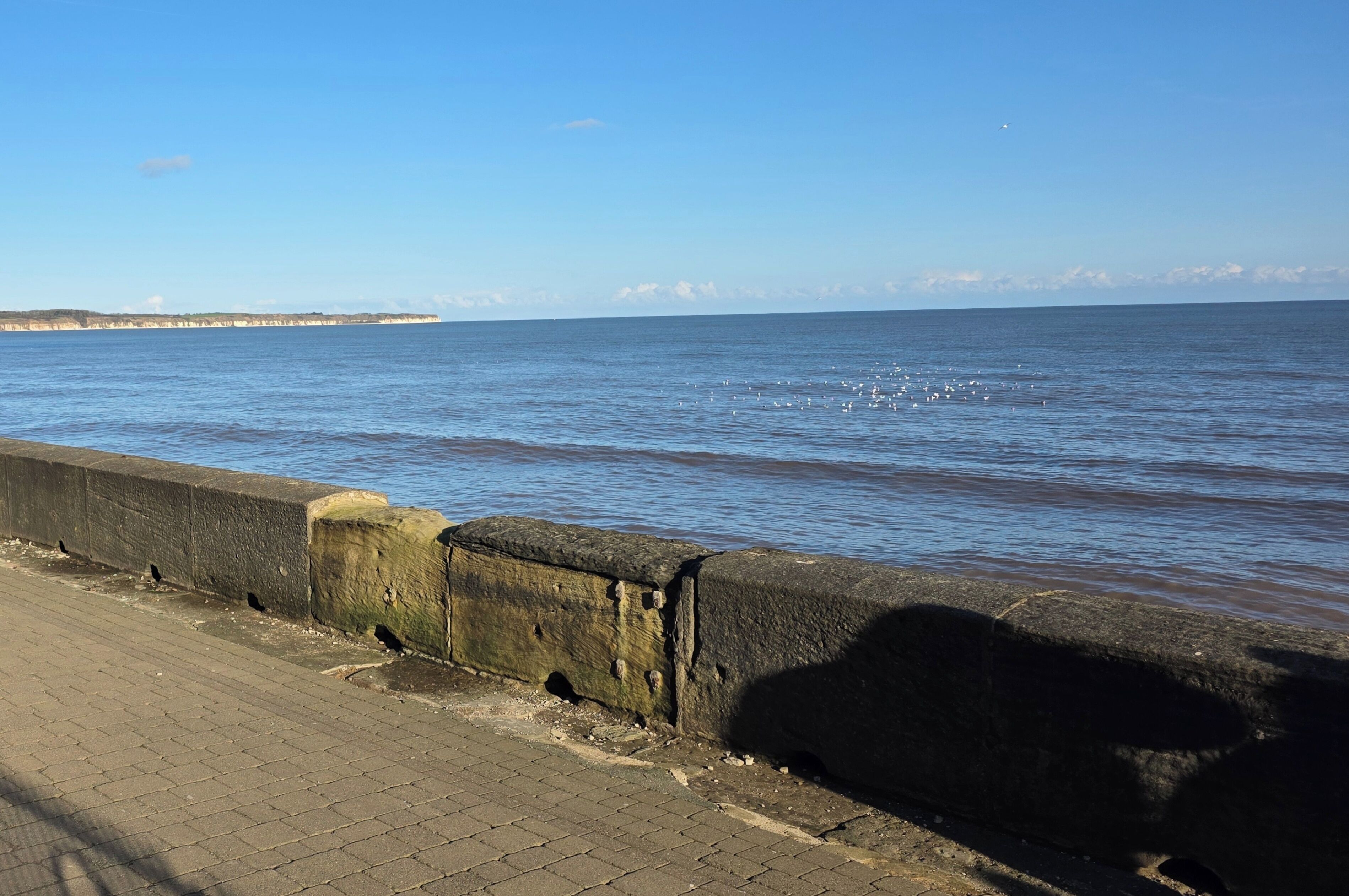 A coastal walkway with a concrete barrier and a view of the sea.