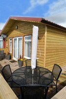 A wooden cabin with a patio featuring a round table and chairs, a covered seating area, and a sliding glass door.