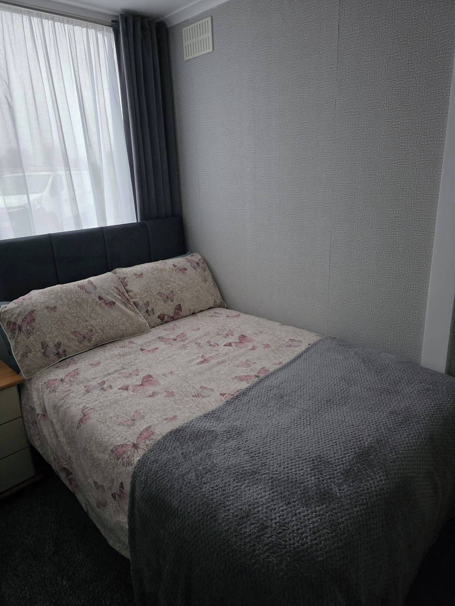 Un dormitorio pequeño y ordenado con cama, una ventana con cortinas y una pared con textura.