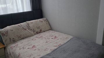 Un dormitorio pequeño y ordenado con cama, una ventana con cortinas y una pared con textura.