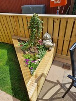A wooden planter box with a variety of flowers and a small statue of a figure.