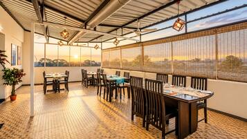 A restaurant with a terrace, tables, chairs, and a view of the sunset.