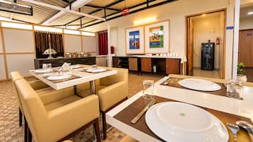 A dining area with tables set for two, a kitchen in the background, and a fire extinguisher on the wall.