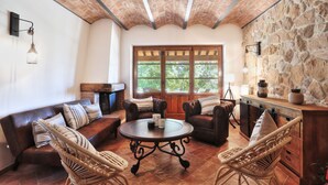Un salon chaleureux avec un mur en pierre, une cheminée, des canapés en cuir et des fauteuils en osier.