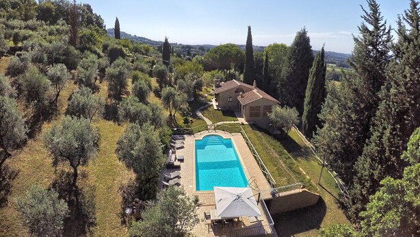Vue aérienne d’une propriété dotée d’une piscine, entourée d’arbres et bordée d’une colline.