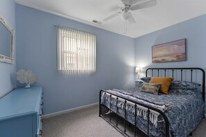 Een slaapkamer met een bed, een plafondventilator, een raam met zonwering en een schilderij aan de muur.