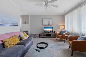 Ein modernes Wohnzimmer mit einem grauen Sofa, einem braunen Ledersessel, einem Flachbildfernseher und einem Deckenventilator.