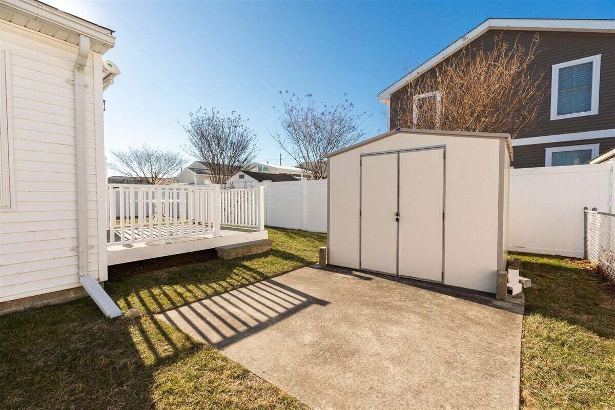 Een achtertuin met een wit hek, een tuinhuis en een woning.