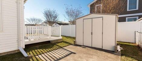 A residential backyard with a white fence, a shed, and a house.