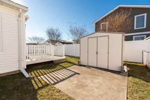 Un patio trasero residencial con cerca blanca, un cobertizo y una casa.