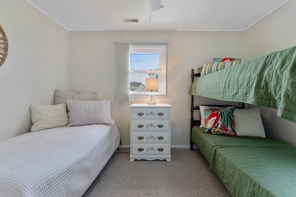 Une chambre avec deux lits, une commode et une fenêtre.