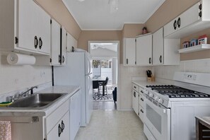 A kitchen with white cabinets, a stainless steel sink, a stove, and a dining area visible through an open door. - Newly Redecorated Beach Home in Wildwood Crest (Wildwood Crest)