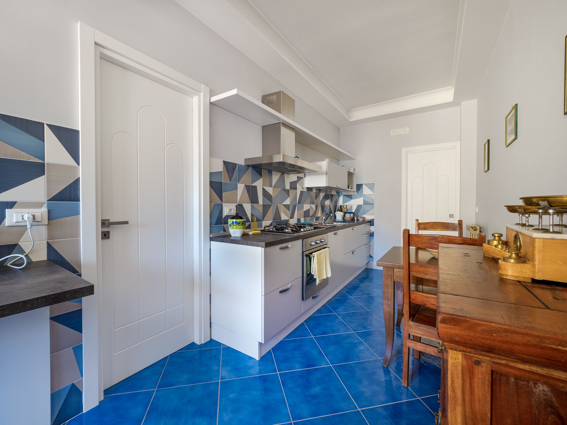 Une cuisine moderne avec un sol carrelé de bleu, des meubles blancs et une table à manger en bois.