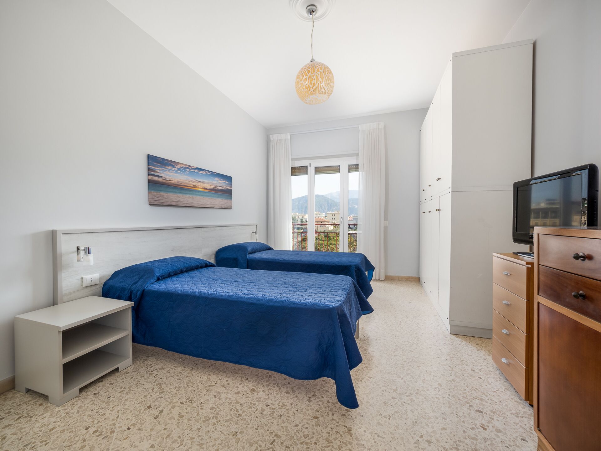 Une chambre avec deux lits, une télévision, une armoire et un tableau au mur.