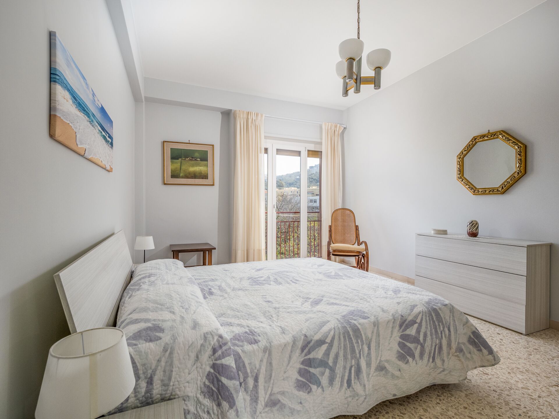 Ein Schlafzimmer mit Bett, Kommode, Stuhl und Blick ins Freie.
