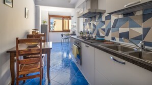 Cocina moderna con comedor, que cuenta con un amplio ventanal, salpicadero de azulejos geométricos y electrodomésticos de acero inoxidable.