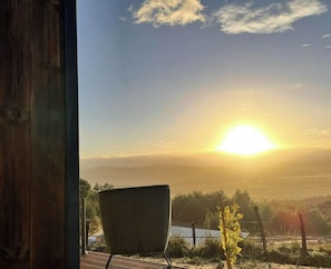 A view from a window overlooking a sunset, with a chair and a small plant visible in the foreground.