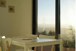 A dining area with a white table and chairs, a window with a view of a cityscape, and two framed pictures on the wall.