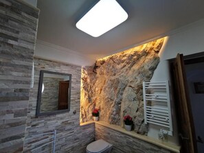 A bathroom with a stone wall, a mirror, a toilet, and a towel rack.