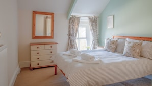 A bedroom with a bed, a dresser, a mirror, and a window with curtains. - Berry Hall - Porty Eynon (Swansea)