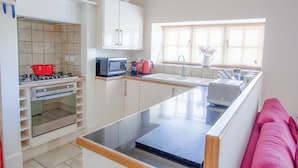 A modern kitchen with a built-in oven, microwave, and gas stove. There is a window with blinds, a sink, and a countertop with a toaster. - Berry Hall - Porty Eynon (Swansea)