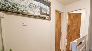 Un couloir avec des portes en bois, un tableau accroché au mur et un escalier doté d’une rampe blanche.