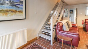 Un escalier menant à l’étage supérieur, un canapé en cuir rouge, une petite table en bois et un tableau représentant un paysage, encadré, accroché au mur.
