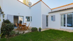 A modern house with a patio, a dining area with wooden chairs and a table, and a sliding glass door leading to a bedroom. - Cosy family house for 6 in Les Portes en Ré (Les Portes-en-Ré)