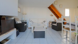 A modern living room with a white sofa, two wicker chairs, a white coffee table, and a TV. A wooden staircase leads to an upper level. - Cosy family house for 6 in Les Portes en Ré (Les Portes-en-Ré)