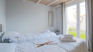 A hotel room with two beds, a large window with curtains, a mirror on the wall, and a bedside table with a lamp. - Cosy family house for 6 in Les Portes en Ré (Les Portes-en-Ré)