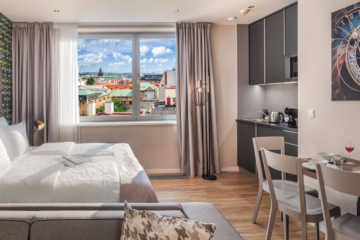 Quarto de hotel moderno com uma cama grande, vista para a cidade, cozinha compacta e área de refeições.