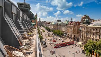 A view from a balcony overlooking a city square with historic buildings, a red tram, and a clear sky.