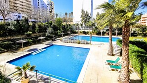Un espace piscine comprenant deux piscines, entouré de palmiers et de chaises longues.