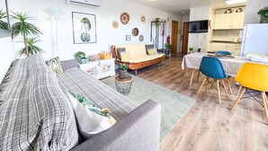 Un salon avec un canapé, une table à manger avec des chaises et, au fond, un coin cuisine.