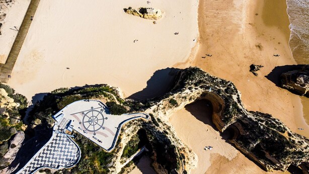 Vue aérienne d’une plage avec une grande formation rocheuse aux contours irréguliers.
