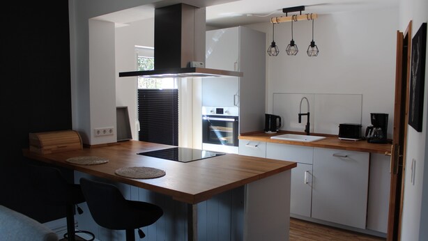 A modern kitchen with a wooden island, bar stools, a built-in oven, and pendant lights. - Cottage in Kluess (Güstrow OT KLueß)