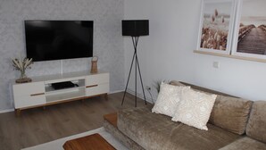 A modern living room with a flat-screen TV, a floor lamp, a sofa, and a coffee table. - Cottage in Kluess (Güstrow OT KLueß)