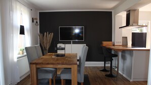 A modern kitchen with a wooden table and chairs, a built-in oven, and a TV mounted on the wall. - Cottage in Kluess (Güstrow OT KLueß)