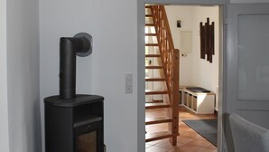 A modern living room with a wood-burning stove, a staircase leading to a dining area, and a grey sofa. - Cottage in Kluess (Güstrow OT KLueß)