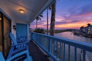 A balcony with blue chairs, a door, and a view of a water body with buildings in the background. - Canal-Front Escape | Pool, Hot Tub & Water Views (Corpus Christi)
