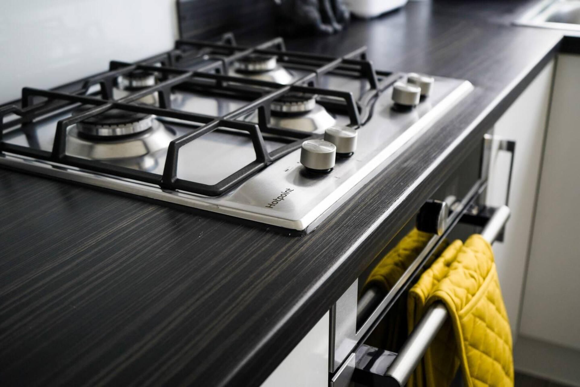Una cocina con estufa a gas, campana extractora de acero inoxidable y una toalla amarilla en un perchero.