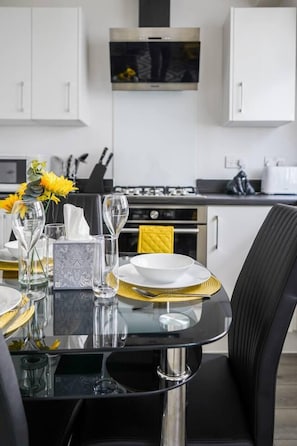 A modern kitchen with white cabinets, a stainless steel stove, and a dining area with a glass table set for two. - Livestay- Perfect For Contractors Luxury Apartment (Slough)