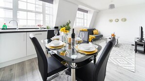 A modern kitchen with a dining table set for four, a sofa, and a TV in a living area. - Livestay- Perfect For Contractors Luxury Apartment (Slough)