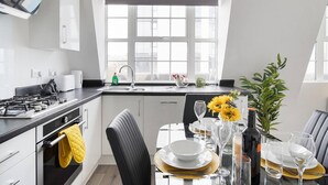 A modern kitchen with a gas stove, sink, and a dining area set for a meal. - Livestay- Perfect For Contractors Luxury Apartment (Slough)