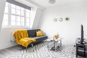 A modern living room with a grey sofa, a yellow throw blanket, a coffee table, and a TV stand. - Livestay- Perfect For Contractors Luxury Apartment (Slough)