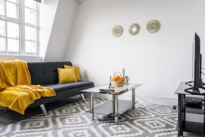 A modern living room with a dark grey sofa, a yellow throw blanket, a glass coffee table, and a TV on a stand. - Livestay- Perfect For Contractors Luxury Apartment (Slough)