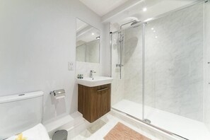 A modern bathroom with a glass shower enclosure, a sink with a wooden vanity, and a mirror above the sink. - Livestay- Perfect For Contractors Luxury Apartment (Slough)